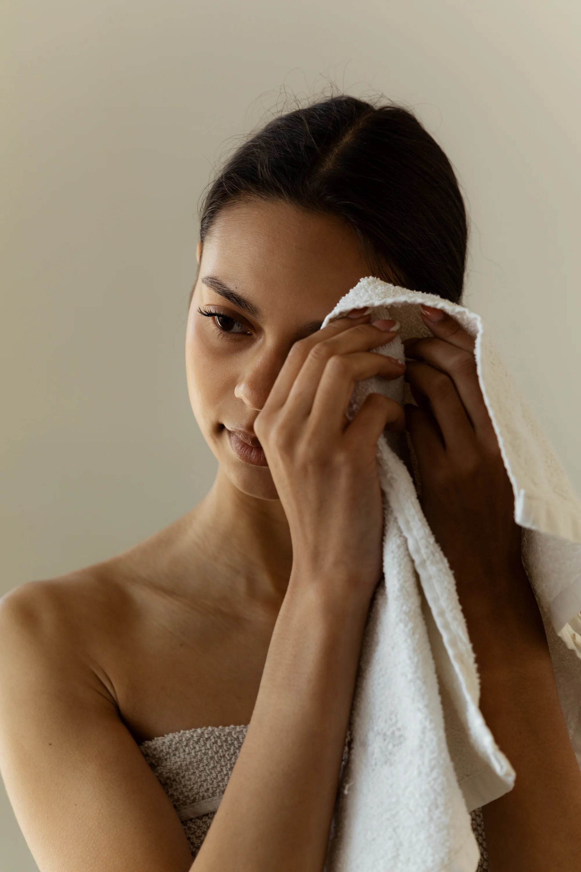 A woman gently pressing a soft white towel to her face after cleansing