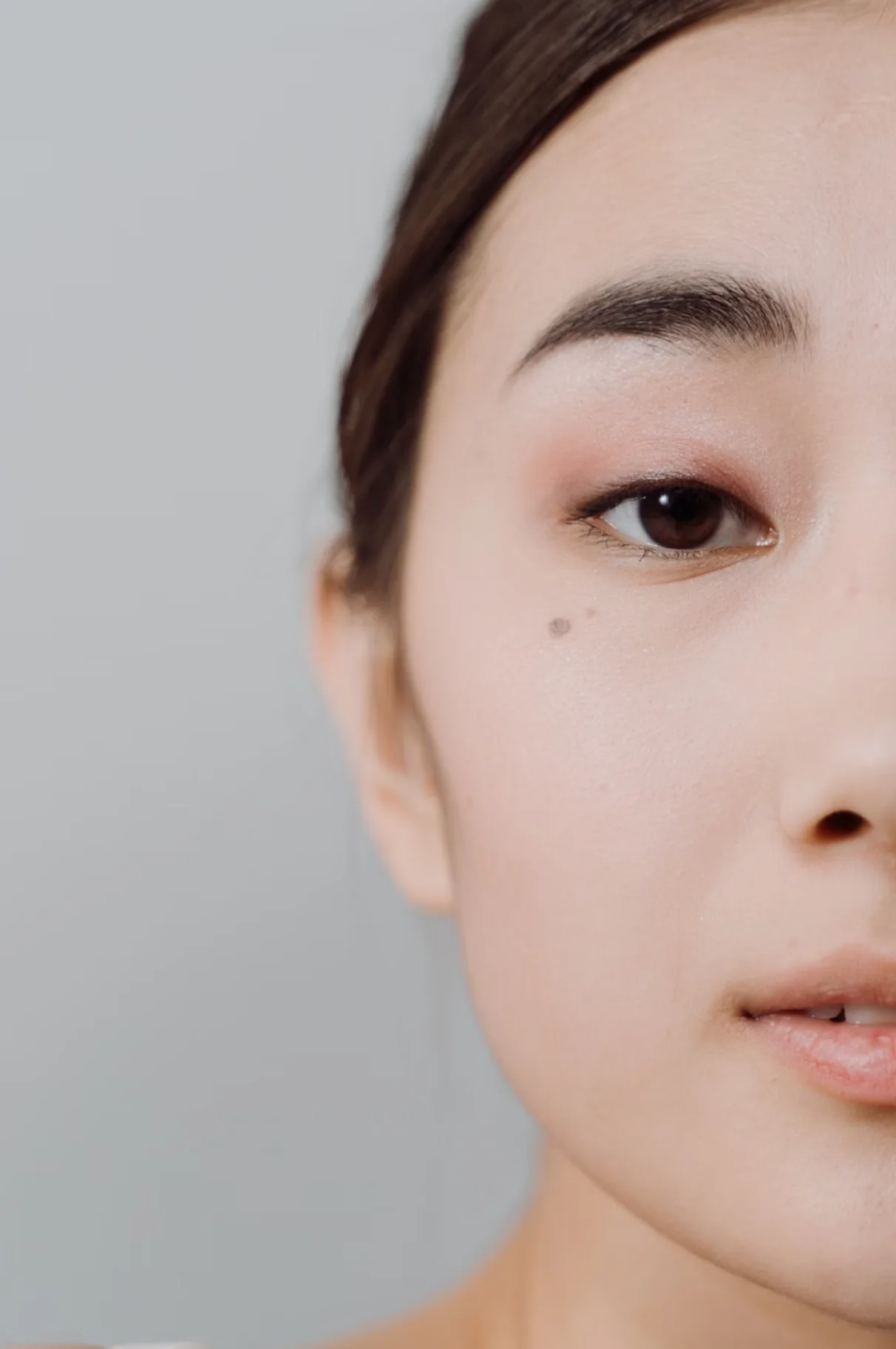 Half-face portrait of a woman with natural, unretouched skin against a soft grey background